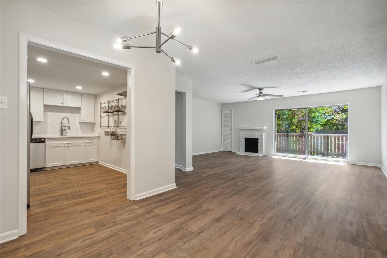 a view of an empty room with wooden floor and a kitchen