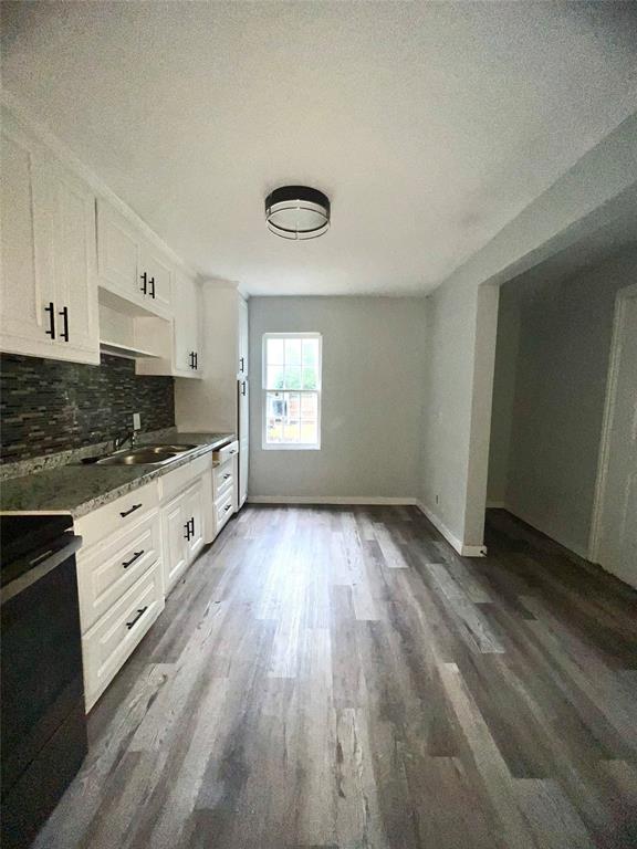 a kitchen with granite countertop a stove a sink and white cabinets with wooden floor