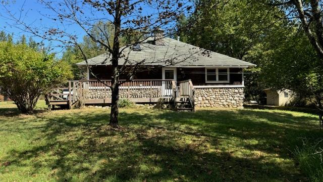 Rear view of property featuring a shed, a wooden deck, and a yard