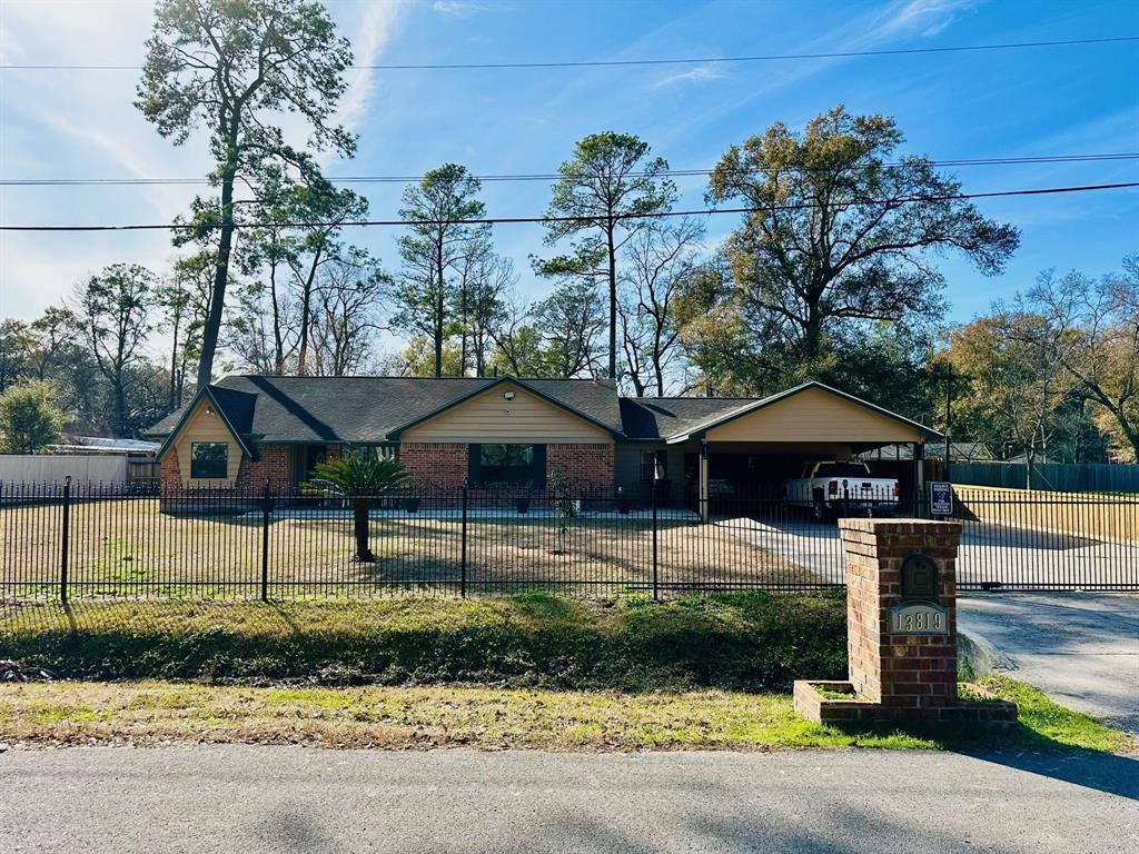 This is a single-story brick home featuring an attached carport, a fenced front yard with a metal gate, and mature trees providing a natural setting. Lot size is over 1/3 of an acre!