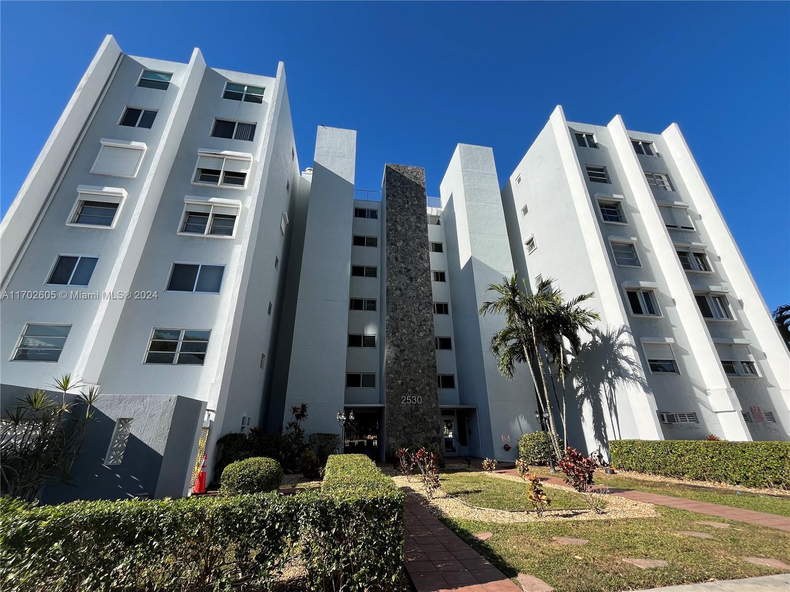 a front view of multi story residential apartment building with yard and parking space