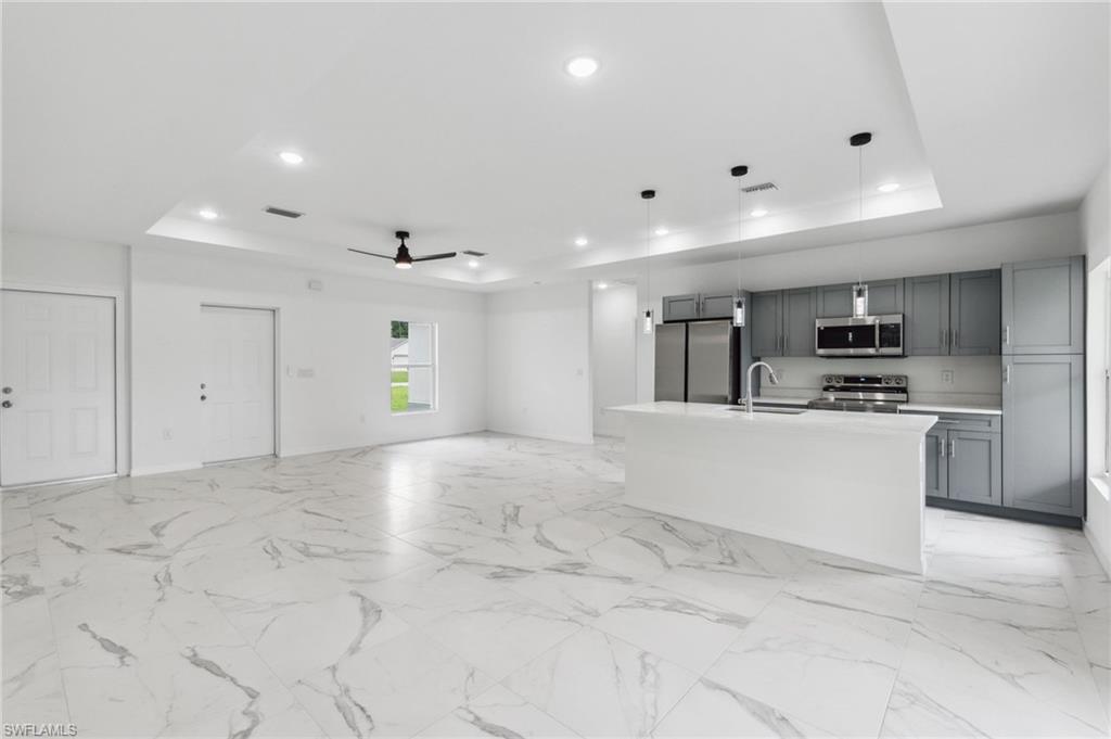 Kitchen featuring a tray ceiling, appliances with stainless steel finishes, an island with sink, and ceiling fan