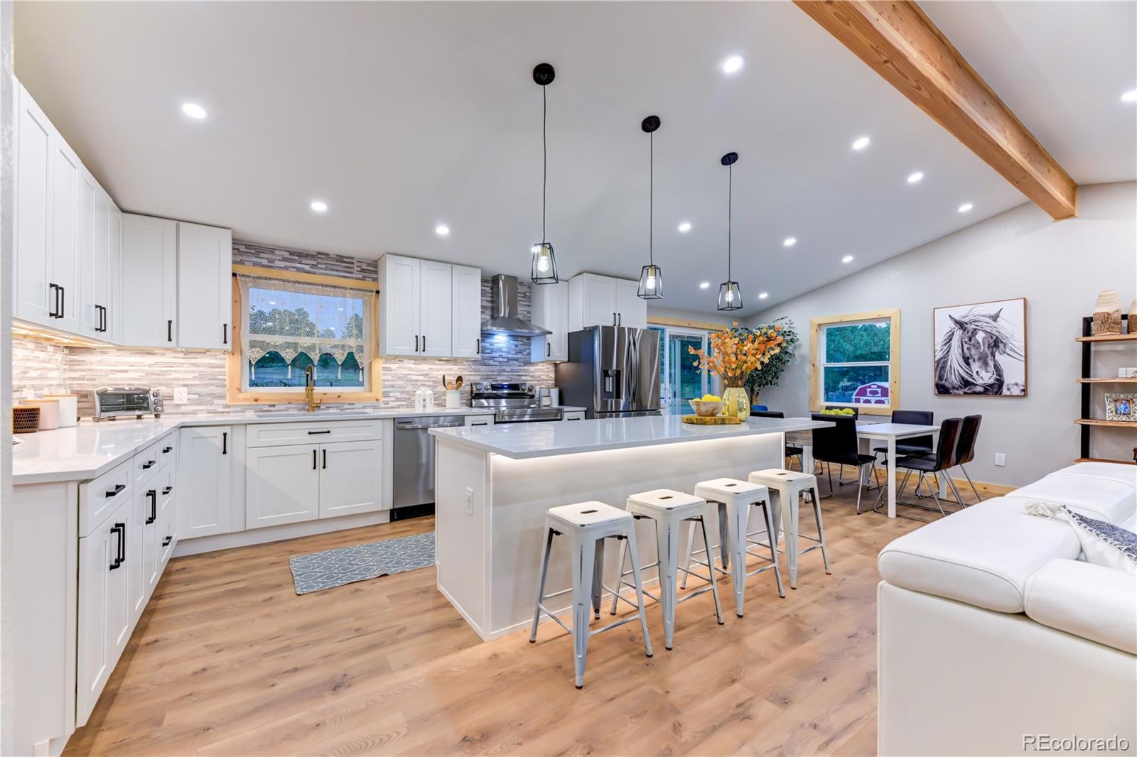 a kitchen with stainless steel appliances kitchen island granite countertop a refrigerator a stove top oven a sink and a dining table with wooden floor