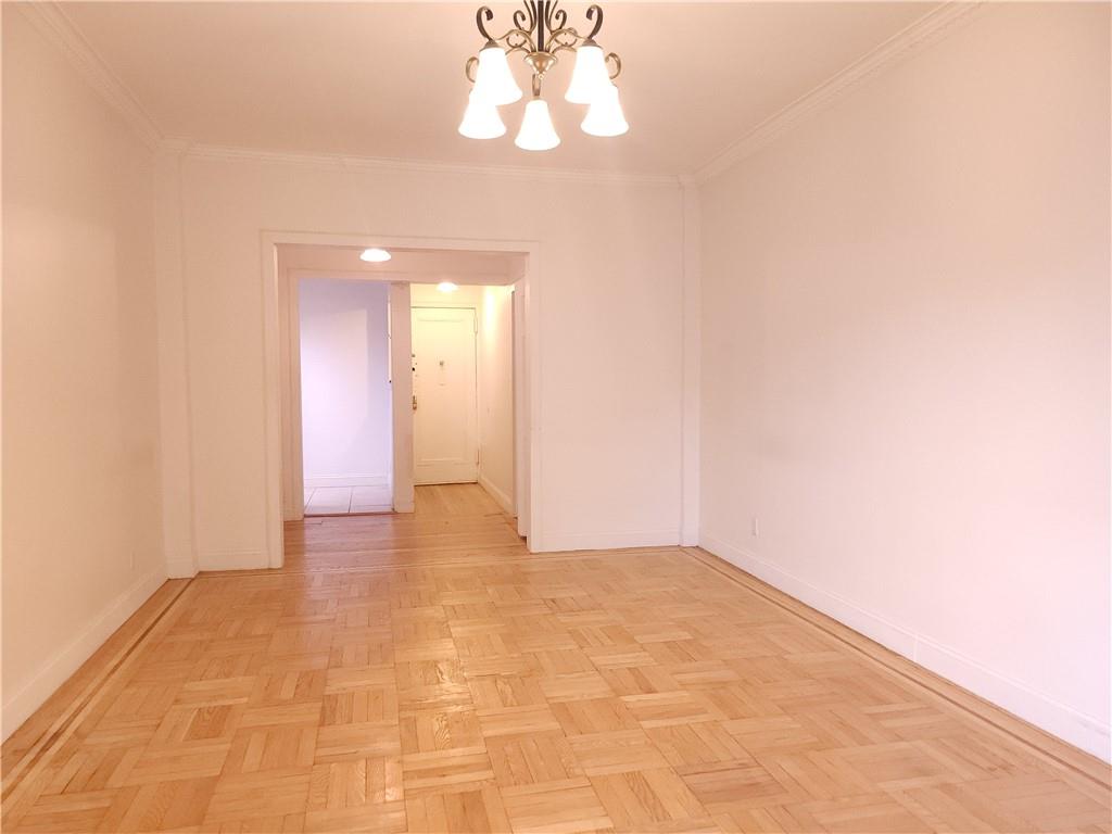 Empty room with an inviting chandelier, light parquet floors, and crown molding