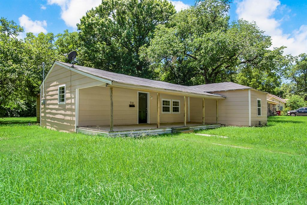 a house that is sitting in the grass with large trees and plants