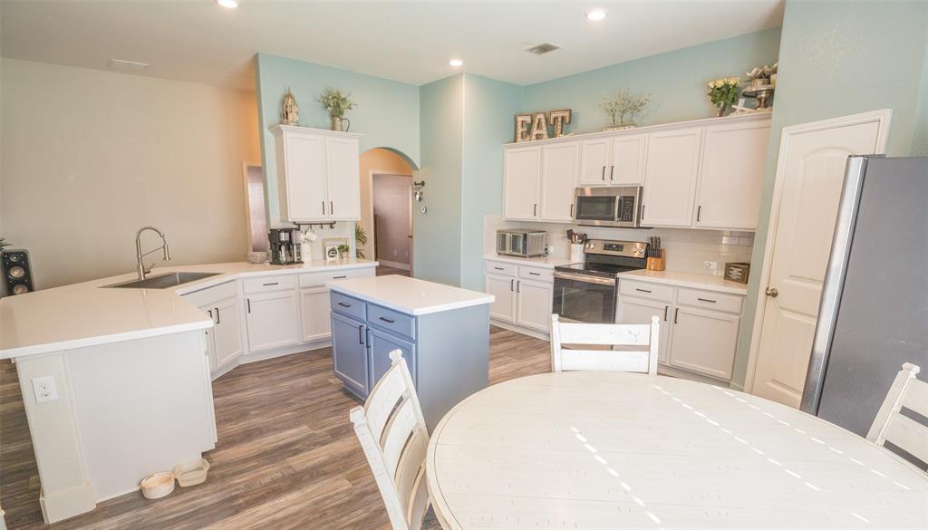 a room with kitchen island a sink a stove a refrigerator and cabinets