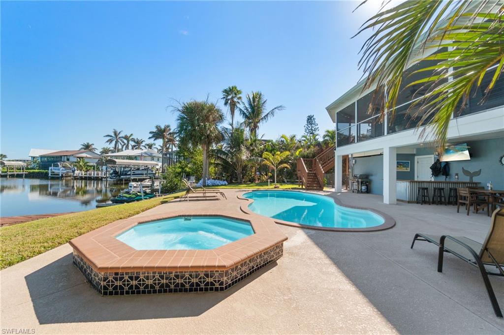 View of swimming pool featuring a grill, an outdoor bar, an in ground hot tub, a water view, and a patio