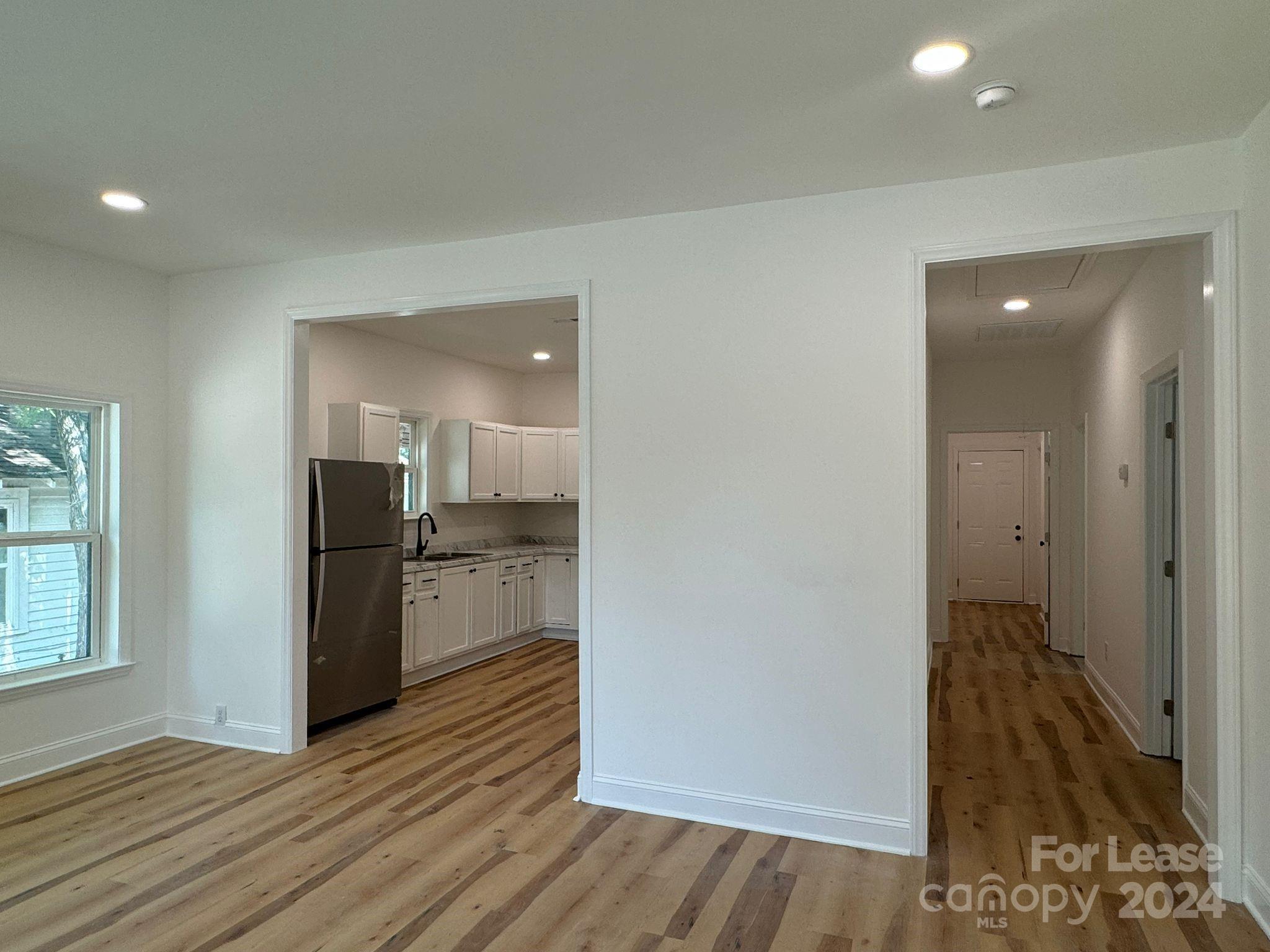 an empty room with wooden floor kitchen view and a living room