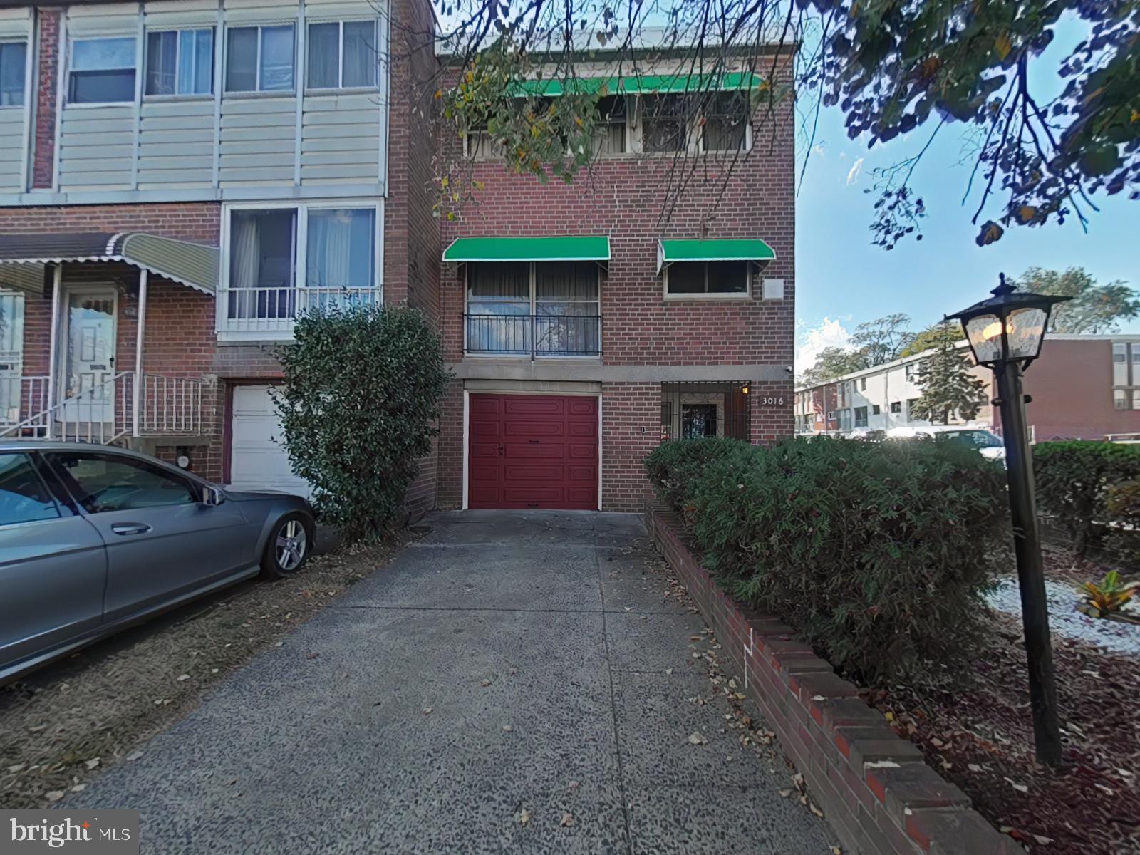 a view of a brick house with a yard plants and large tree