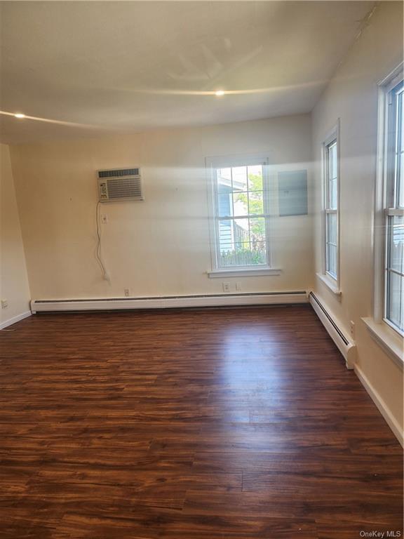 Empty room featuring dark hardwood / wood-style floors, a baseboard heating unit, and an AC wall unit