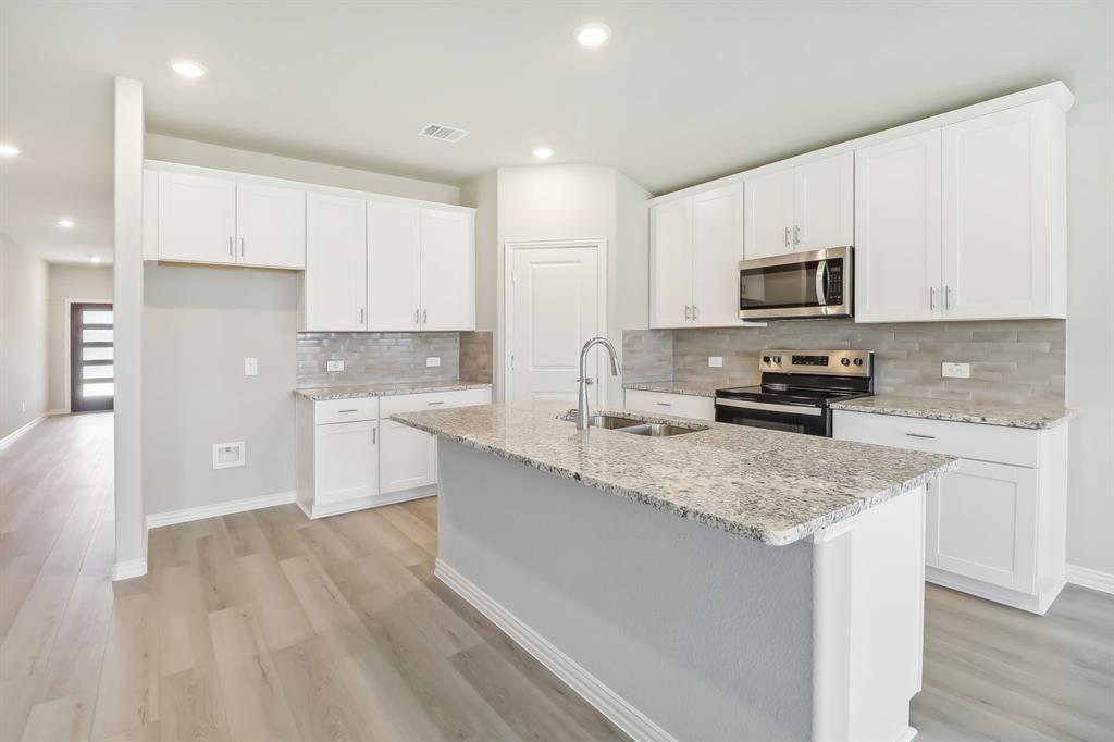 a kitchen with stainless steel appliances granite countertop a sink a stove a microwave a sink a refrigerator with white cabinets and wooden floor