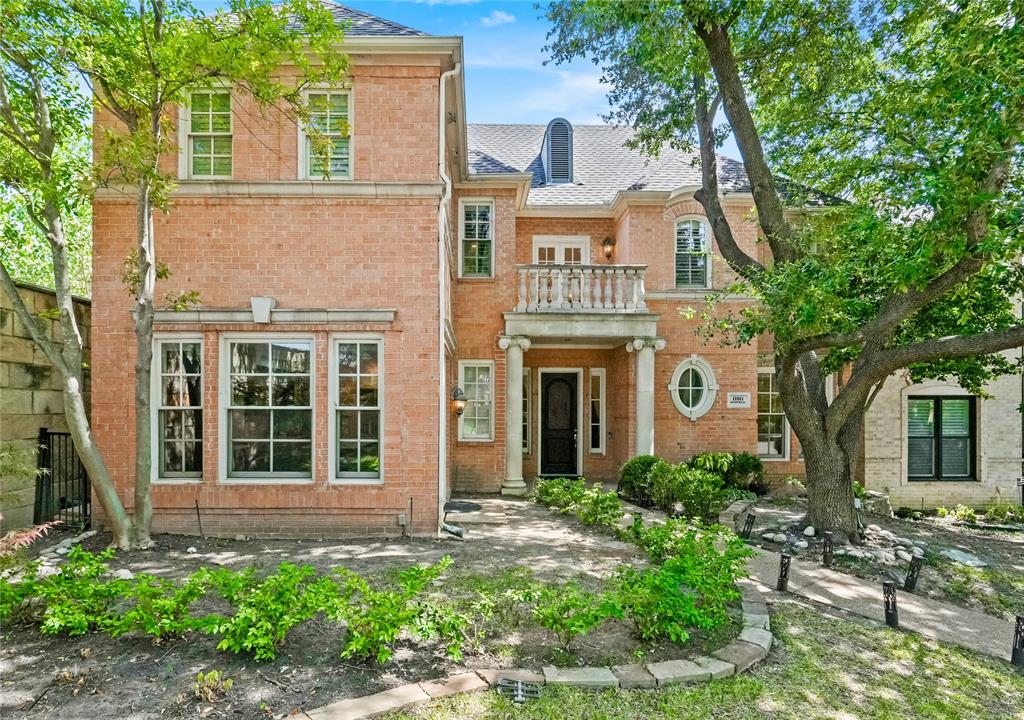 a view of a house with brick walls plants and large tree