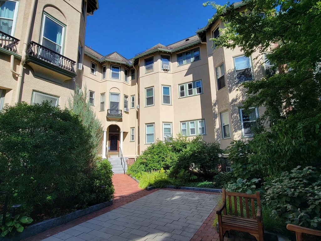 a front view of a multi story residential apartment building with yard and parking