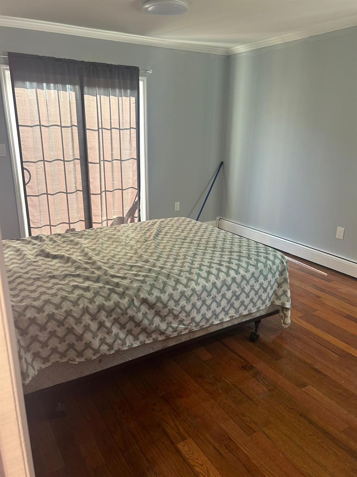 Bedroom featuring a baseboard heating unit, hardwood / wood-style flooring, and ornamental molding