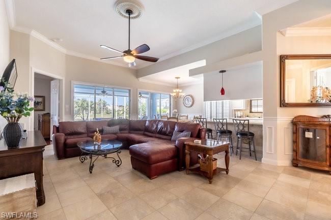 Living room with ceiling fan with notable chandelier, ornamental molding, and light tile patterned flooring