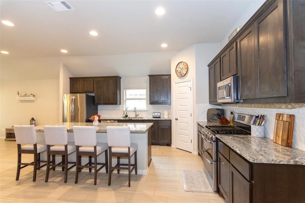 a large kitchen with stainless steel appliances granite countertop a stove top oven a sink a dining table and chairs