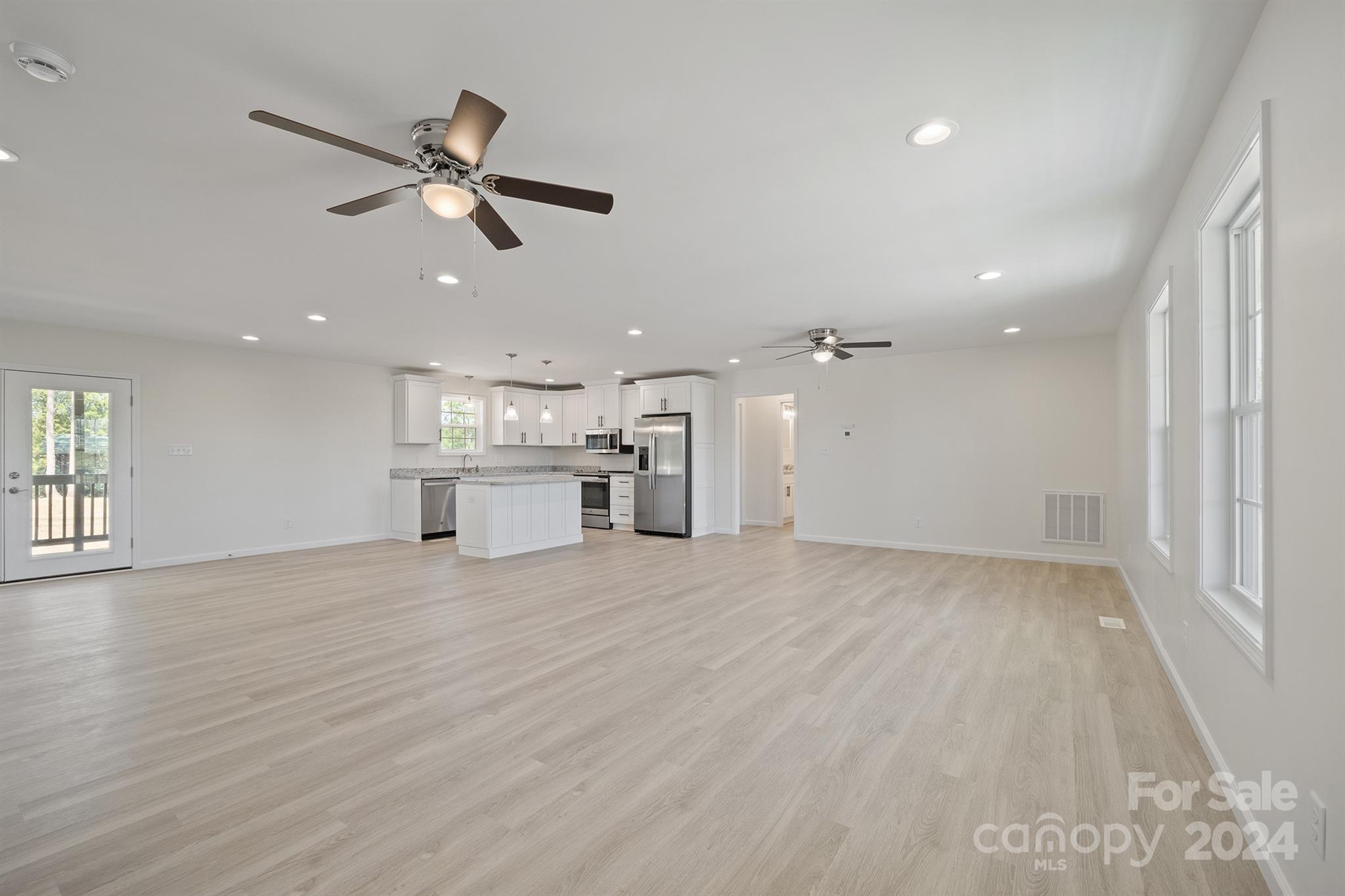 an empty room with wooden floor ceiling fan and windows