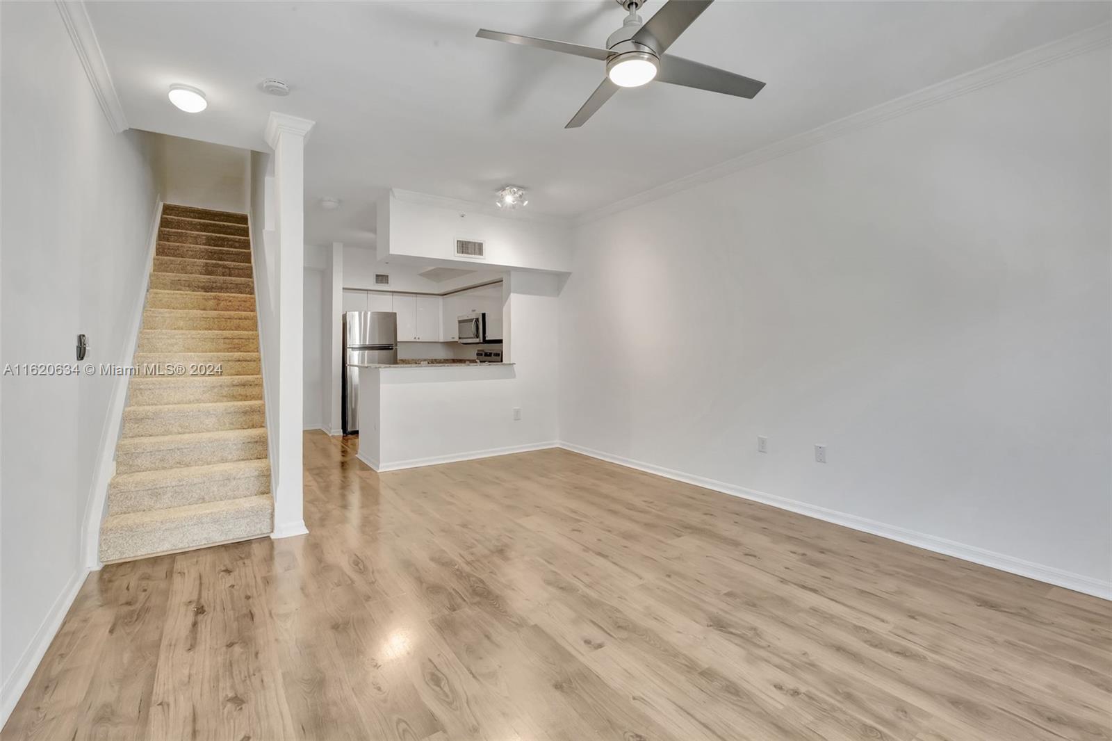 an empty room with wooden floor staircase and kitchen view