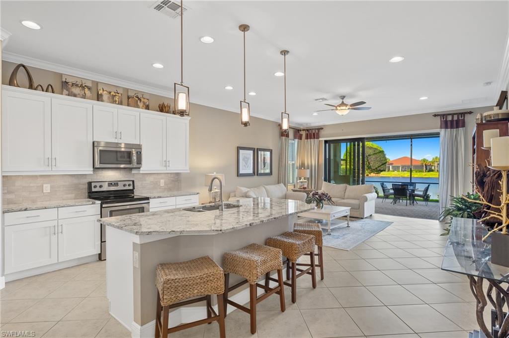 a open kitchen with stainless steel appliances granite countertop a stove top oven a sink dishwasher a dining table and chairs with white cabinets
