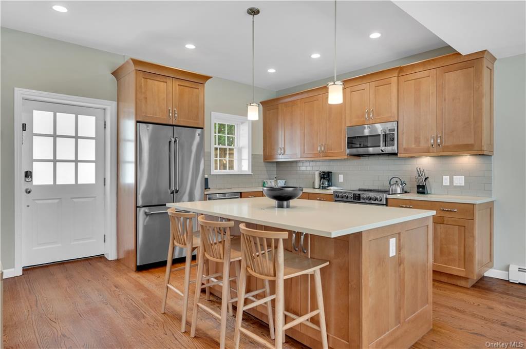 Kitchen featuring light hardwood / wood-style floors, decorative backsplash, decorative light fixtures, stainless steel appliances, and a center island