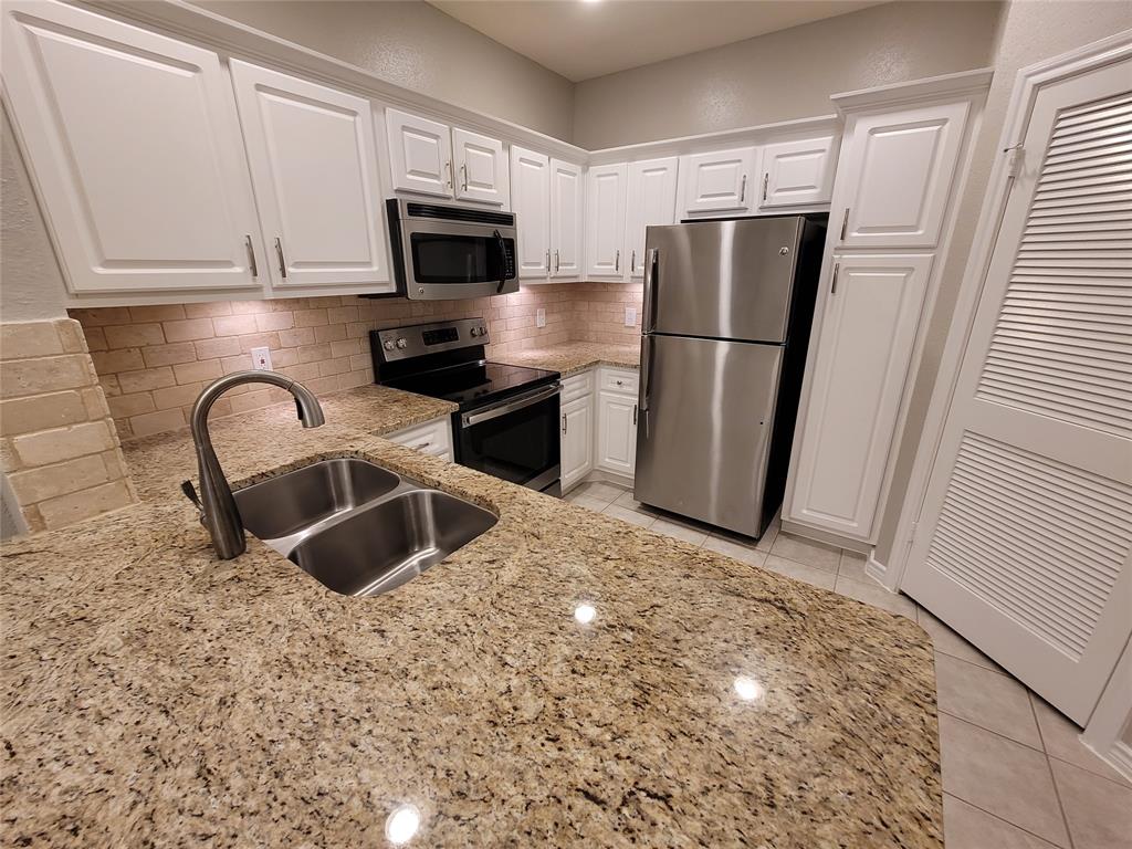 a kitchen with stainless steel appliances granite countertop a refrigerator a stove a sink and a white cabinets