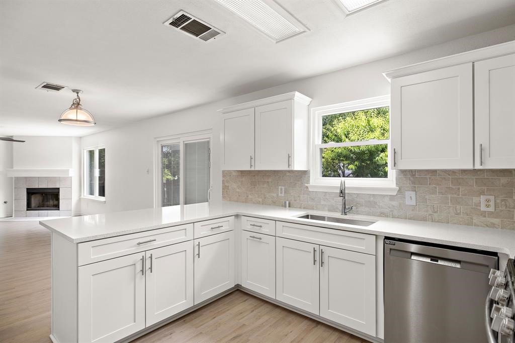 a kitchen with a sink dishwasher and white cabinets with wooden floor