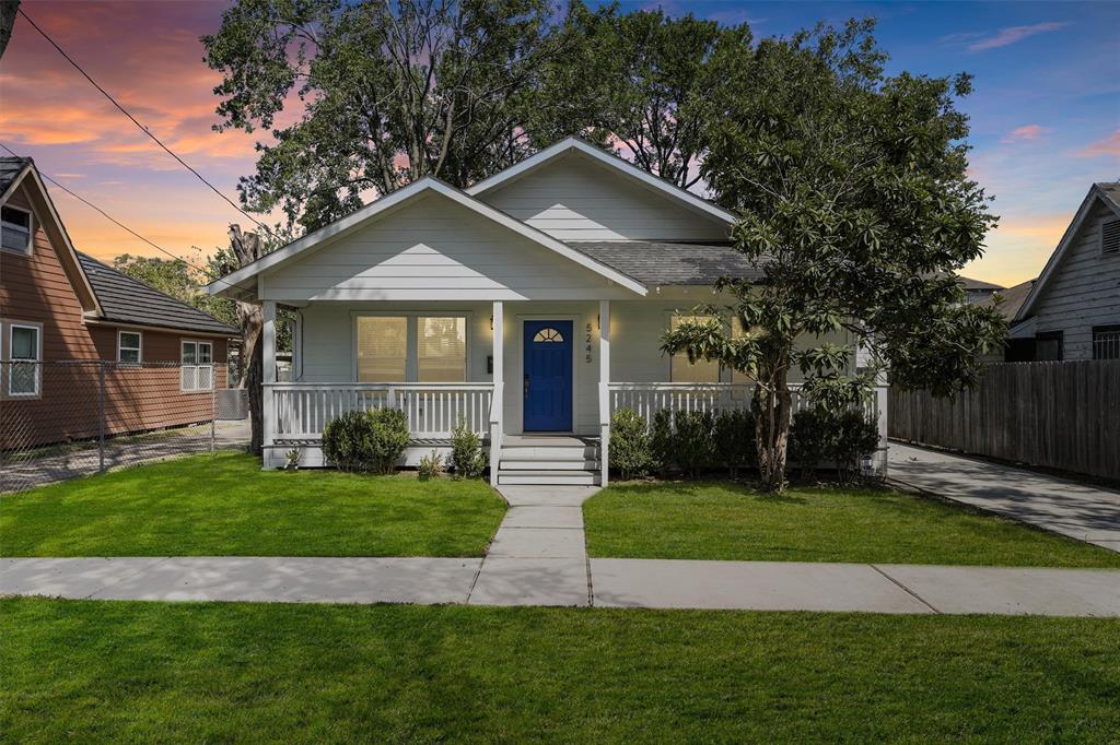 This is a charming single-story home featuring a fresh white exterior with contrasting blue door, a cozy front porch, and well-maintained landscaping. The property includes a fenced yard.