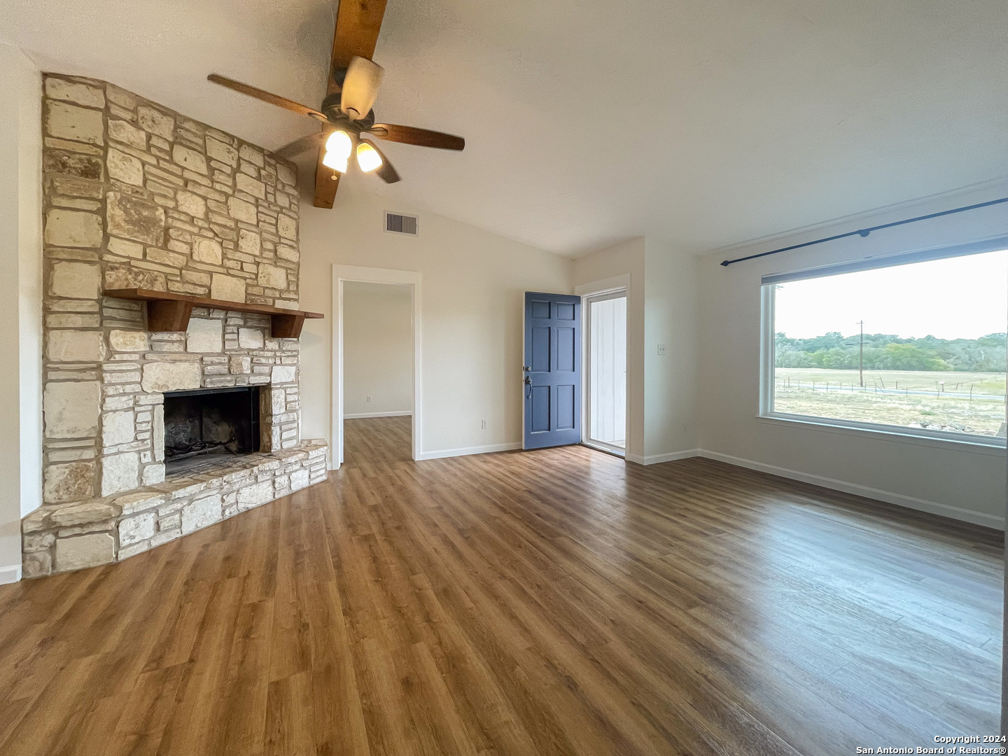 a view of an empty room with wooden floor fireplace and a window