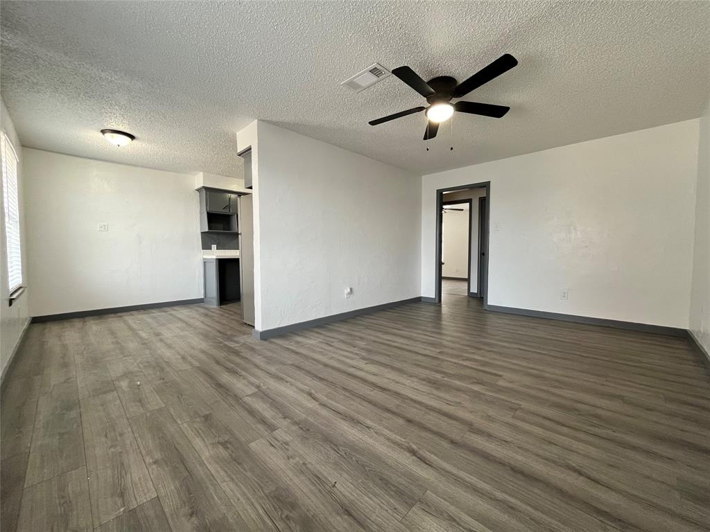 a view of an empty room with wooden floor and a ceiling fan