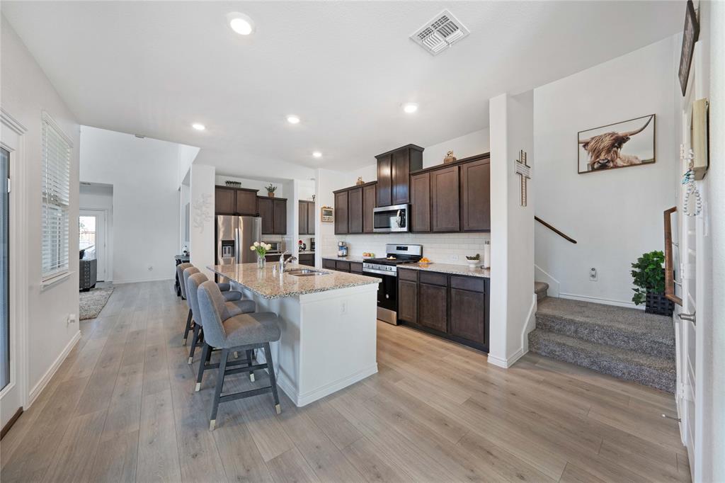 a living room with stainless steel appliances a dining table wooden floor and a kitchen view