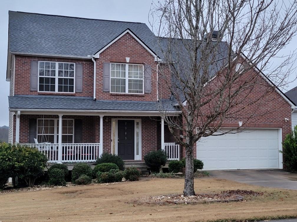 a view of a brick house with a yard plants and large tree