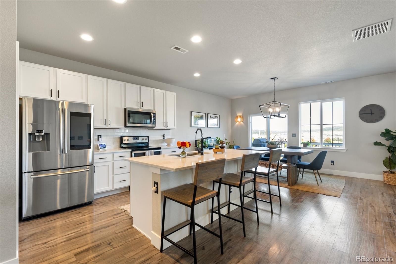 a kitchen with stainless steel appliances granite countertop a refrigerator a stove top oven a sink dishwasher a dining table and chairs with wooden floor