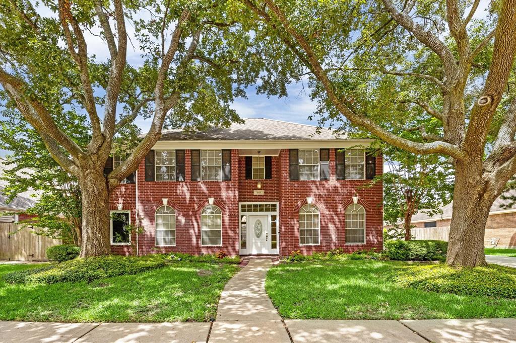 Stunning two-story brick home with mature trees and a well-manicured lawn, offering great curb appeal.