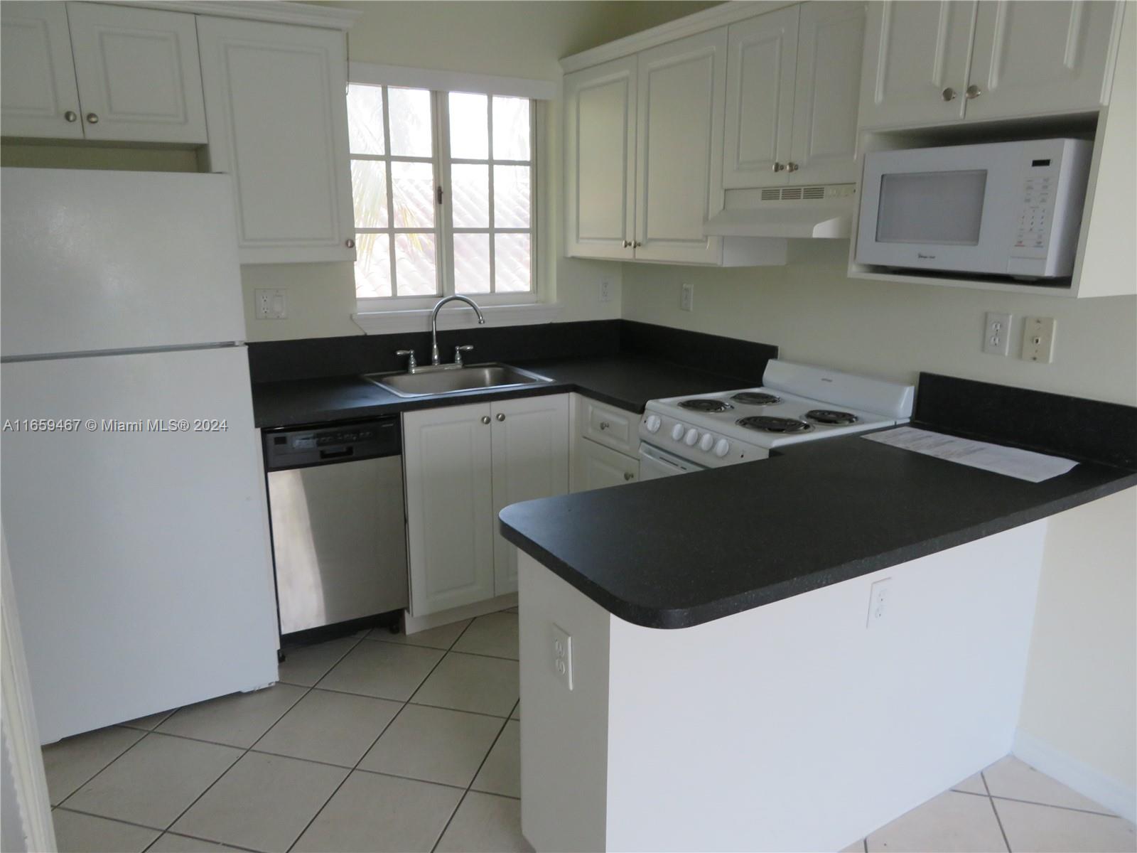 a kitchen with granite countertop a stove a sink a refrigerator and cabinets