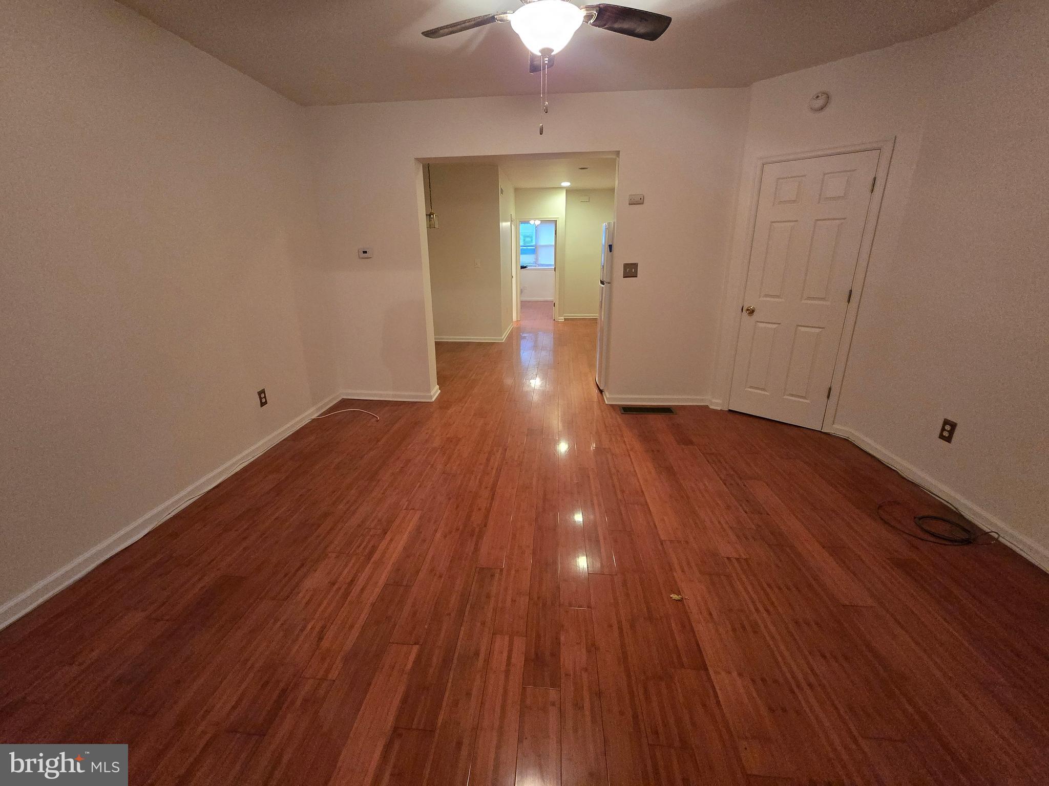 a view of an empty room with wooden floor and a chandelier fan