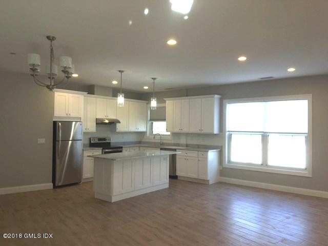 a kitchen with stainless steel appliances kitchen island granite countertop a refrigerator a sink dishwasher a stove and a dining table with wooden floor