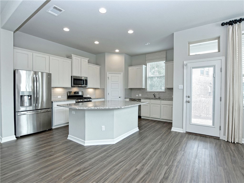 a kitchen with stainless steel appliances a refrigerator a sink dishwasher a stove and white cabinets with wooden floor