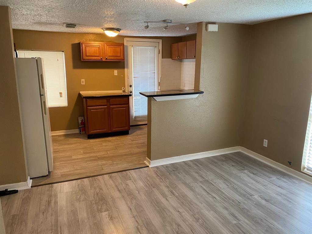 a view of a refrigerator in kitchen and an empty room with wooden floor