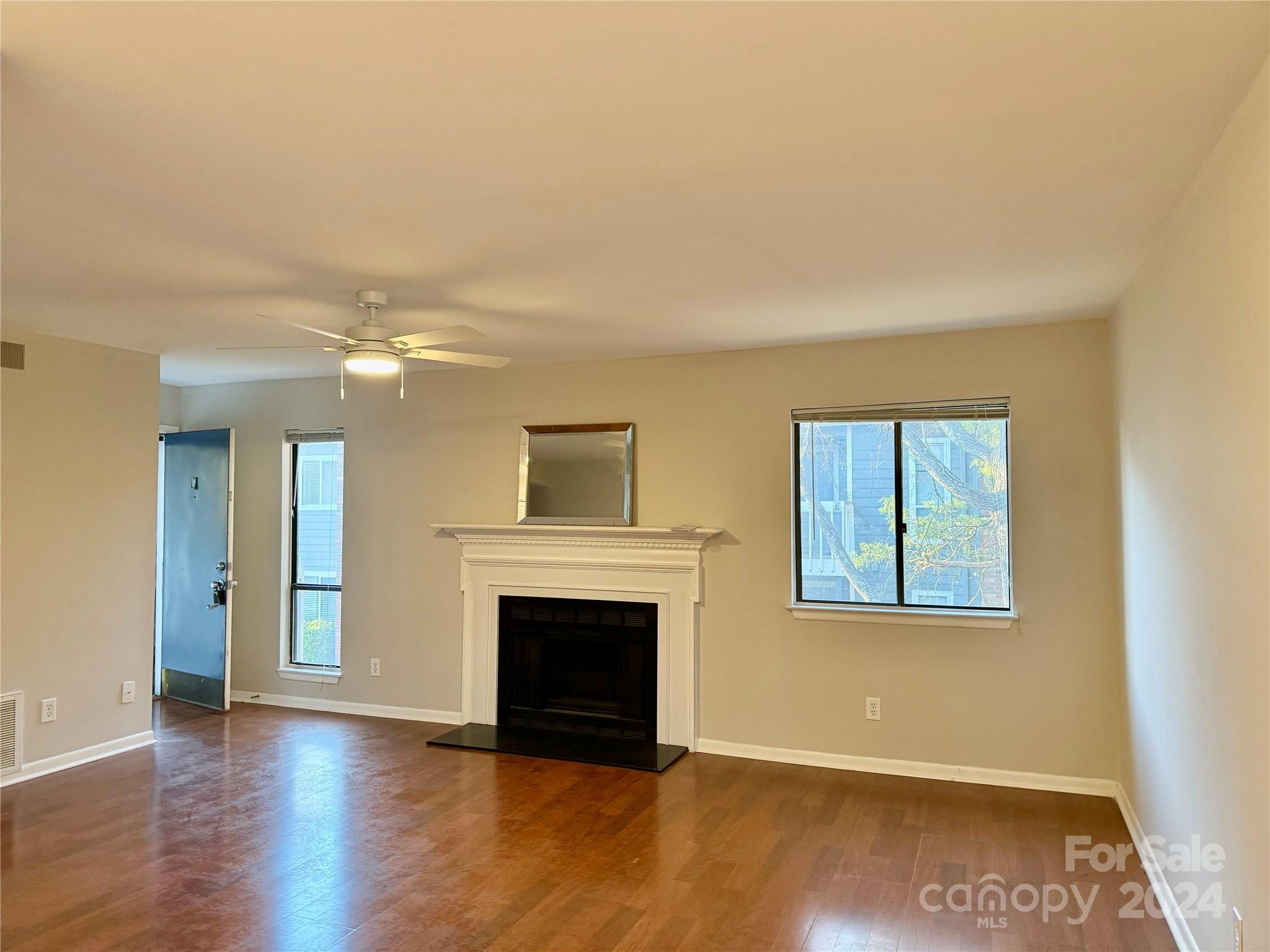 an empty room with wooden floor a fireplace and windows