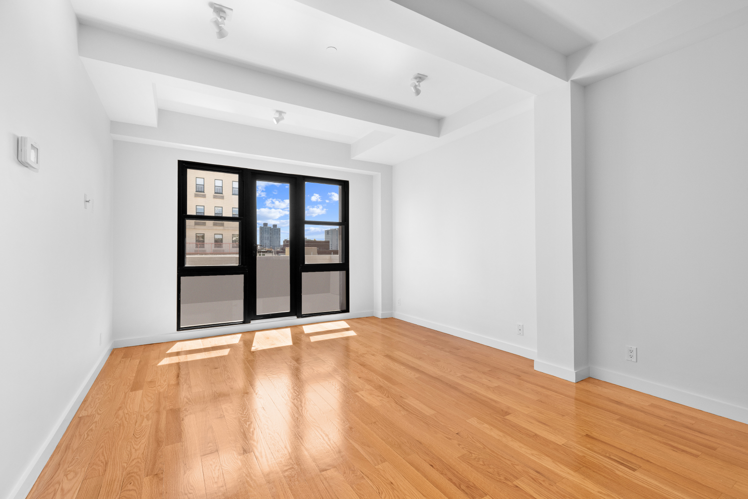 a view of an empty room with a window and wooden floor