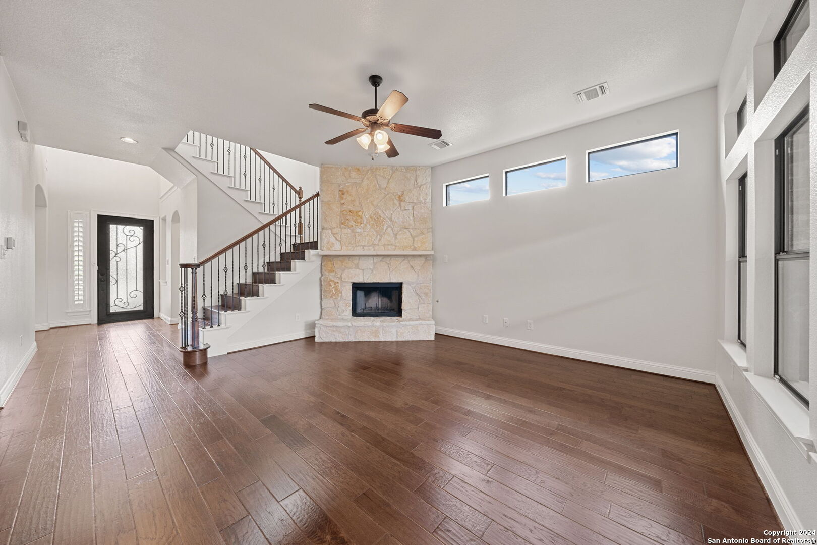 a view of an empty room with wooden floor and a ceiling fan