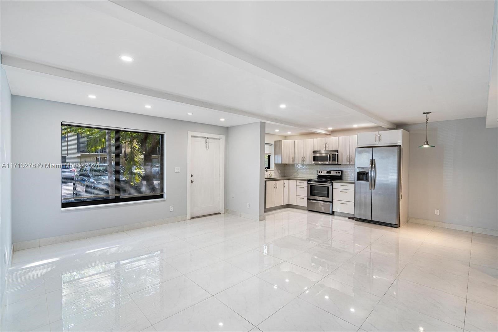 a large white kitchen with stainless steel appliances kitchen island a large window in it