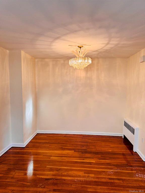 Unfurnished room featuring a chandelier, dark wood-type flooring, and radiator