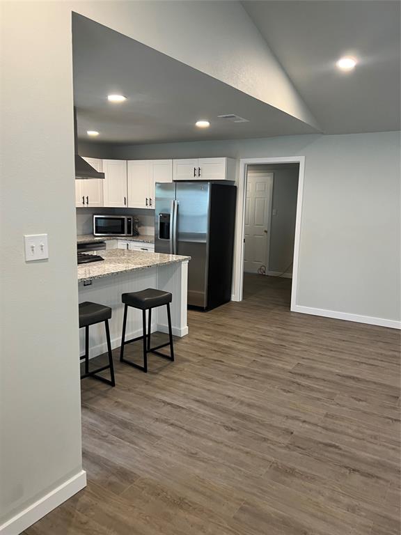 a kitchen with stainless steel appliances kitchen island granite countertop a refrigerator a stove a sink dishwasher and white cabinets with wooden floor