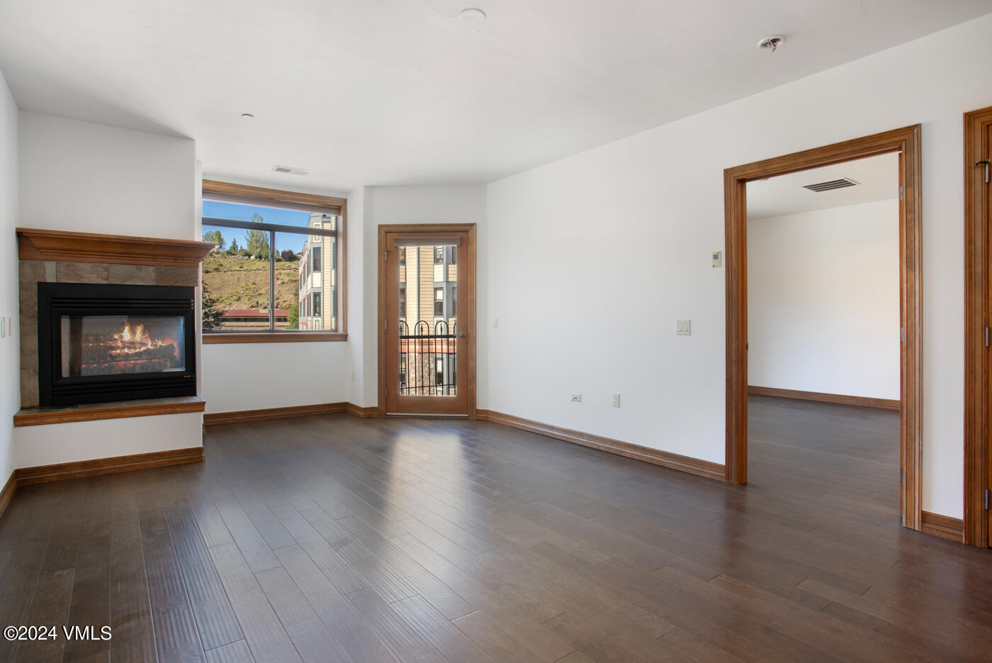 a view of an empty room with wooden floor fireplace and a window