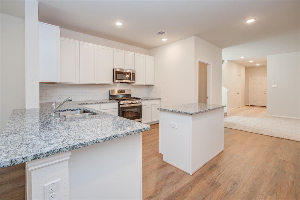 a kitchen with stainless steel appliances granite countertop a sink a stove a microwave a refrigerator a sink and white cabinets with wooden floor