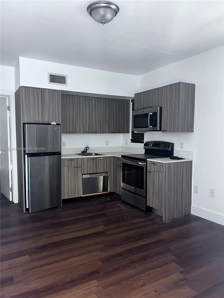 a kitchen with granite countertop a refrigerator stove top oven and wooden floor