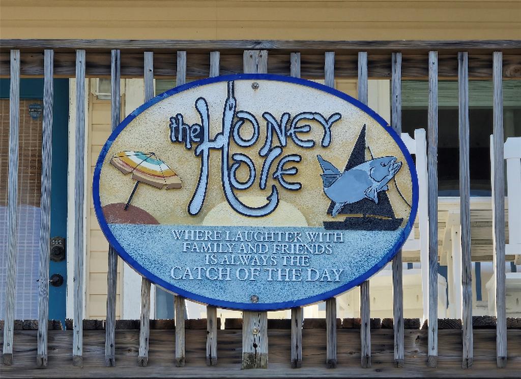 "The Honey Hole" is a friendly and relaxed atmosphere where laughter with family and friends is valued. It is located on the west end of Galveston, in a coastal location. The presence of rocking chairs on the porch adds to the homey and leisurely vibe of the property.