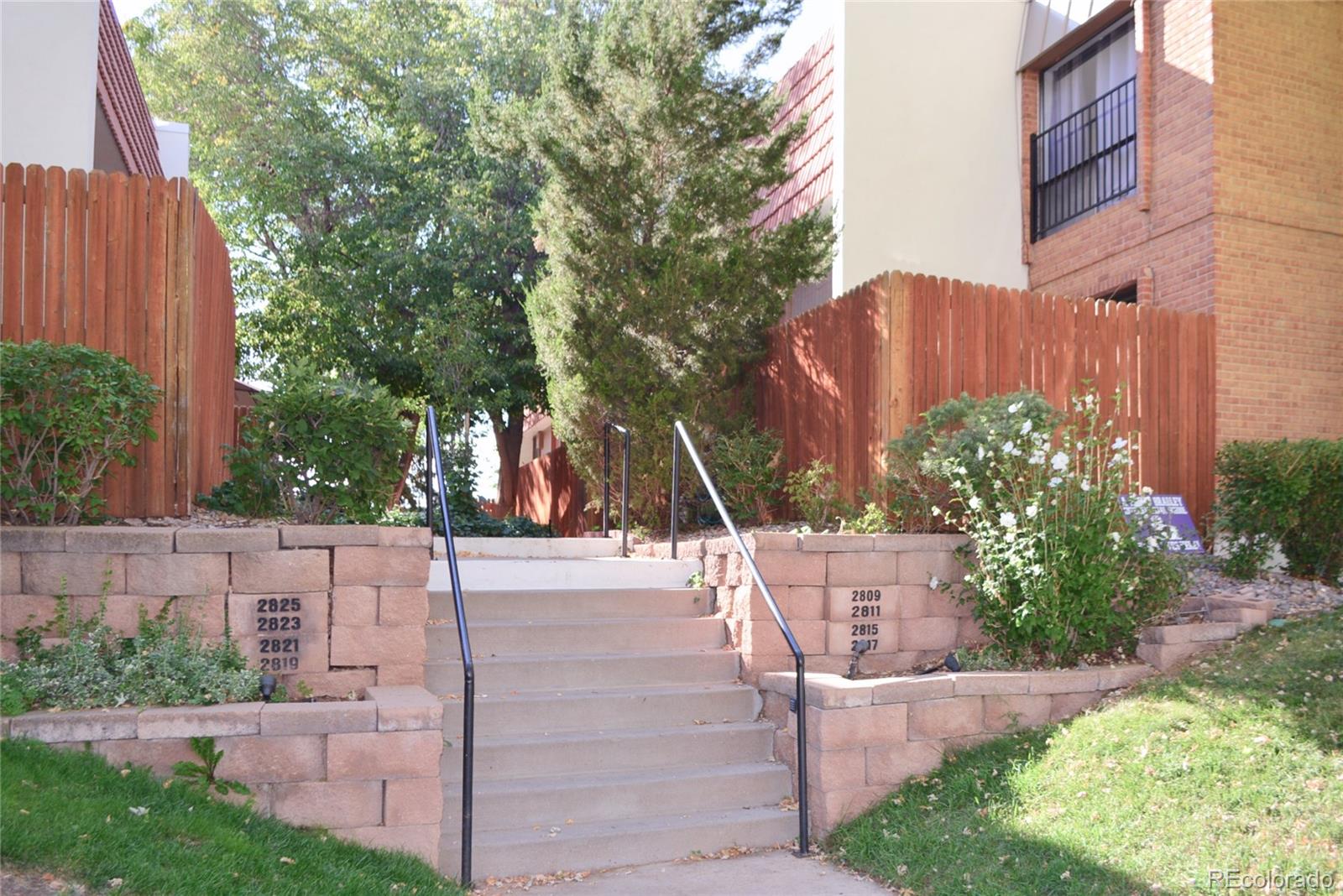 a view of a house with brick walls and a yard with plants and large trees