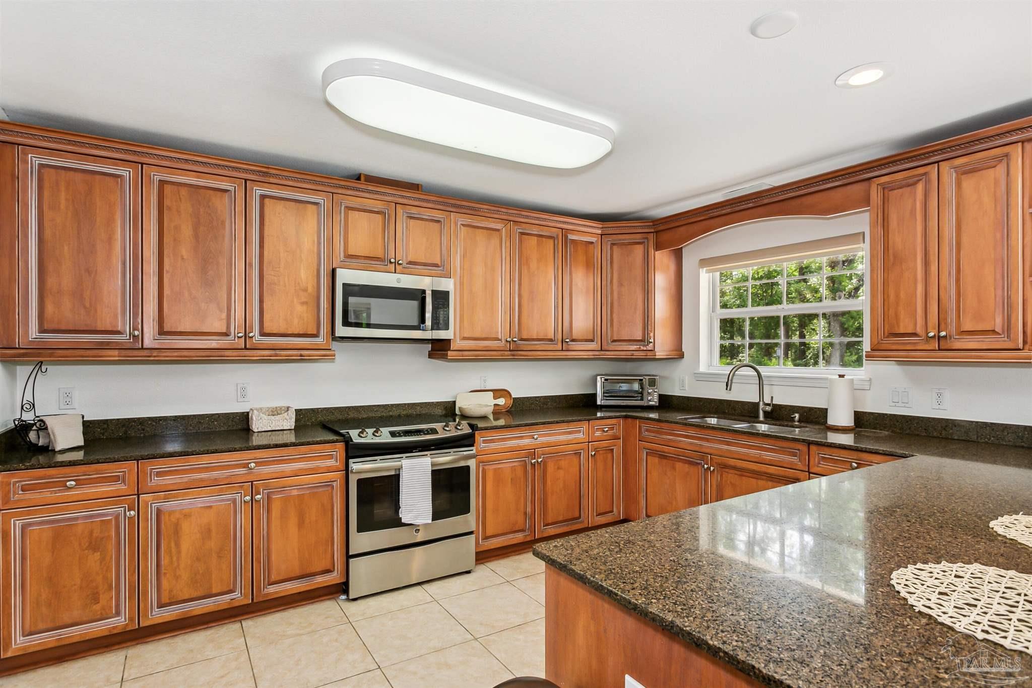 a kitchen with granite countertop stainless steel appliances a sink a stove cabinets and a window